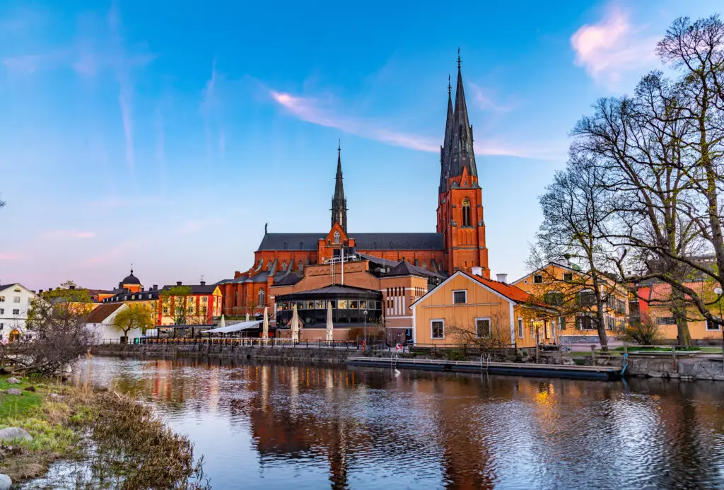 Sunset view of Uppsala Cathedral, a historic landmark reflected on River Fyris in Sweden, capturing the serene beauty and architectural elegance of the site.