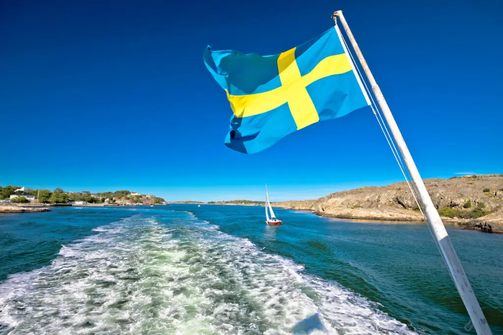Swedish flag waving on a boat in the stunning Gothenburg archipelago with clear blue skies and a view of rocky islands
