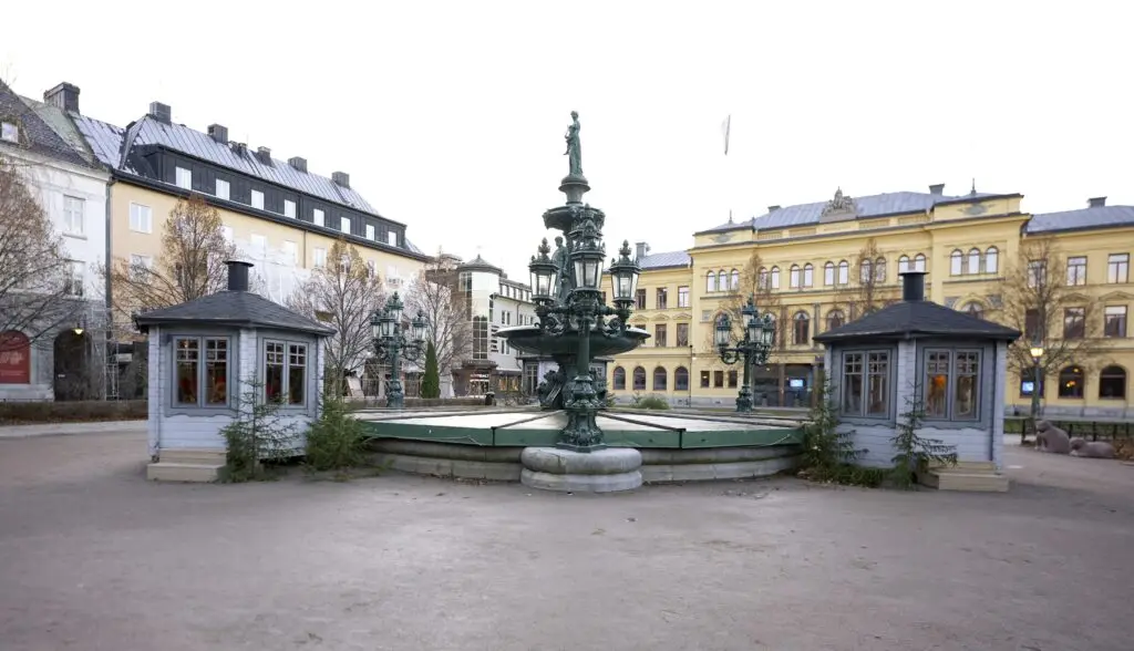 Historic ornate fountain and traditional wooden kiosks in Sundsvall Square, Sweden, showcasing Scandinavian architecture and cultural landmarks.