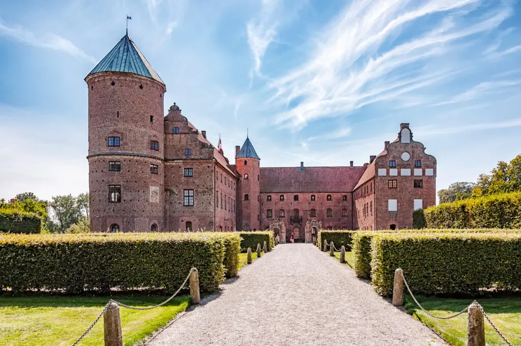 Skarhult Castle in Sweden framed by lush gardens and a stony pathway under a blue sky, a historical icon for Scandinavian tourism.