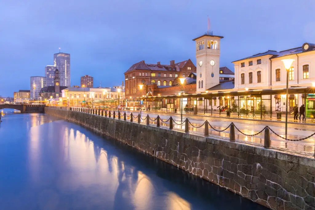 Evening view of Malmo cityscape in Sweden showing the historical architecture and modern buildings with vibrant street lights and reflections on water.