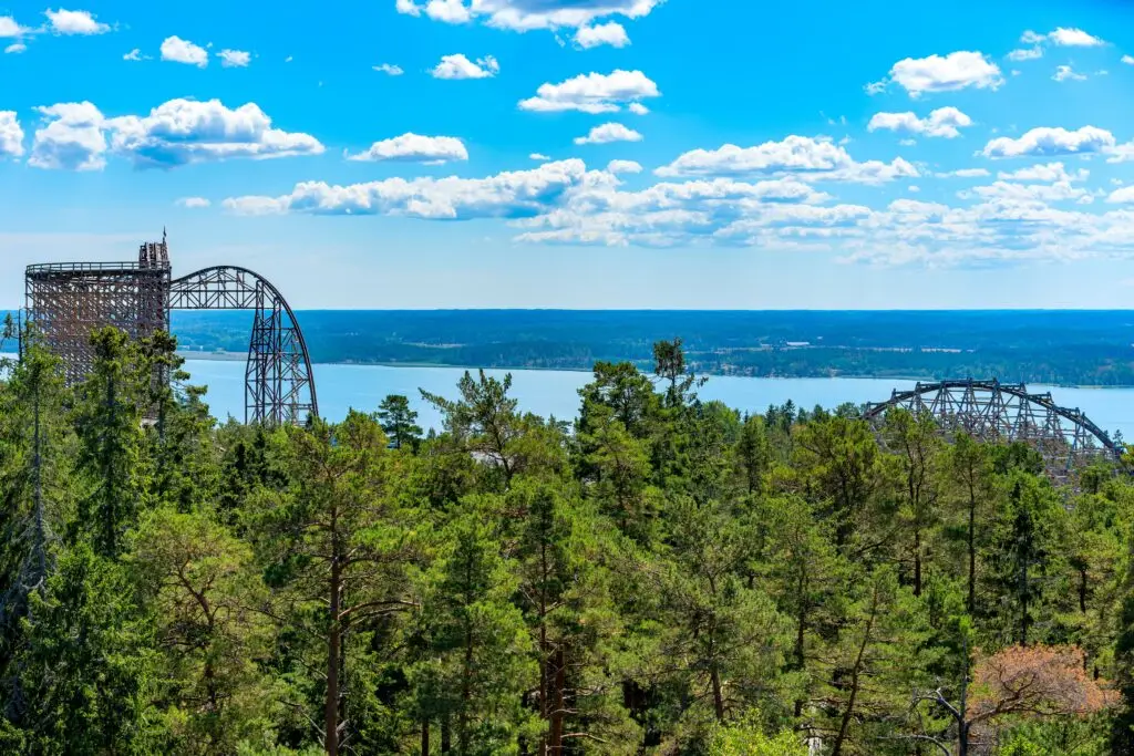 Panoramic view of a large roller coaster at Kolmården Zoo and Amusement Park, overlooking the Baltic Sea and surrounded by dense forests in Sweden.