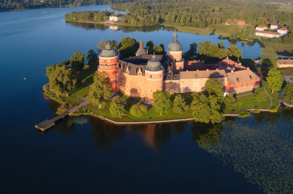 Aerial view of the historic Gripsholm Castle surrounded by lush greenery and calm waters in Mariefred, Sweden, showcasing the architectural beauty and serene landscape ideal for Scandinavian tours.