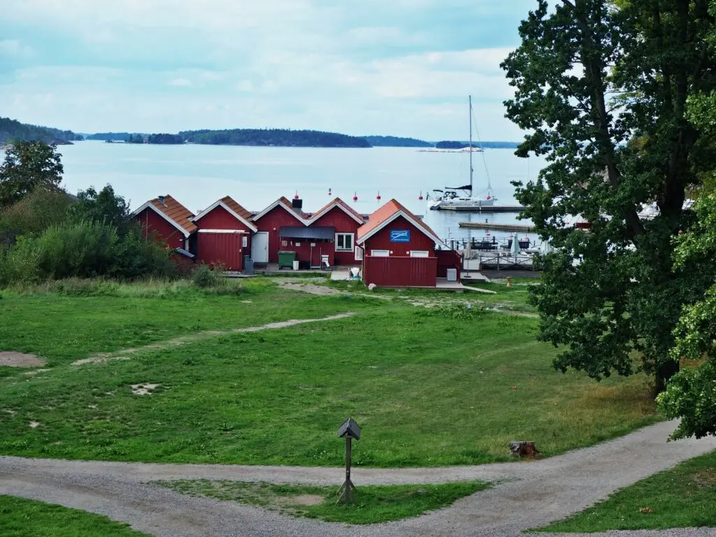 Traditional red chalets and a scenic harbor with a sailing boat on Grinda Island in the Stockholm Archipelago, Sweden, perfect for a tranquil getaway.