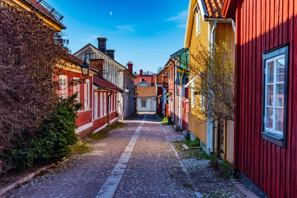 Traditional colorful timber buildings lining a cobblestone street in Gamla Stan, Gavle, Sweden, under a clear blue sky - ideal for Scandinavian cultural tours.