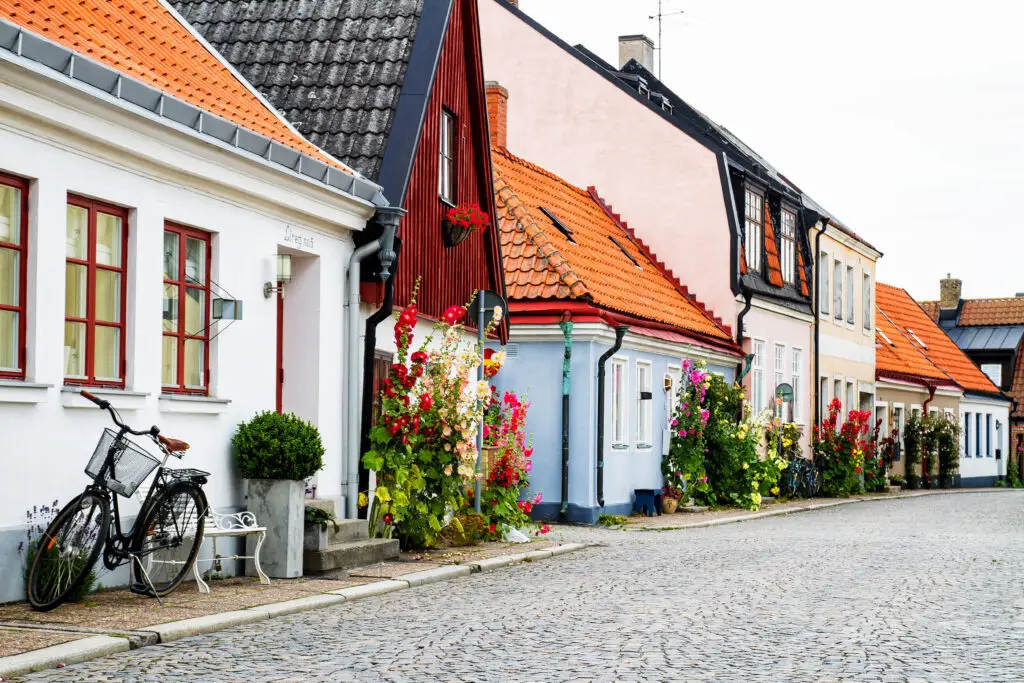 Picturesque view of a cobblestone street in Ystad, Sweden, showcasing colorful traditional houses adorned with vibrant flowers and a bicycle parked along the alley.