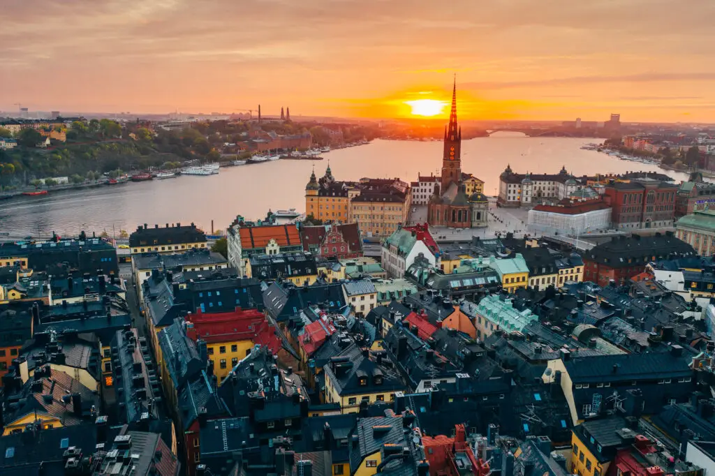 Aerial view of Stortorget in Gamla Stan, Stockholm showcasing the historic colorful buildings and Riddarholmen Church during a stunning sunset.
