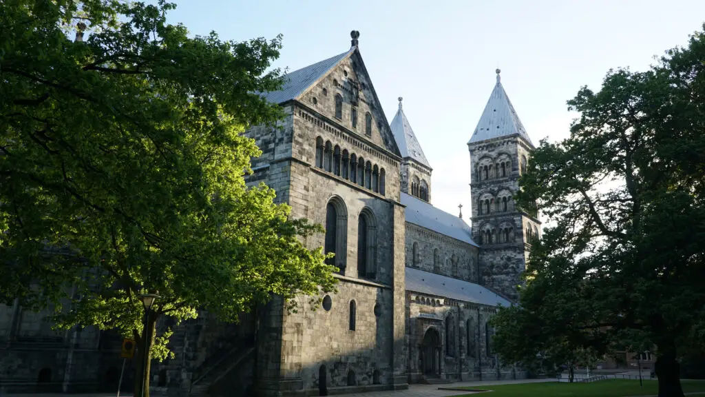 View of Lund Cathedral, a prominent historical and architectural landmark in Lund, Sweden, surrounded by lush green trees under a clear sky.