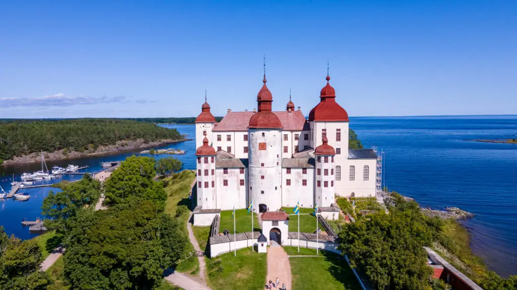Aerial view of Lacko Castle on the shore of Lake Vanern with surrounding lush greenery and moored boats, a popular tourist destination in Sweden.