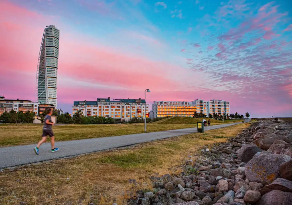 Turning Torso Tower at sunset in Malmo, Sweden, with people enjoying a scenic waterfront walk.