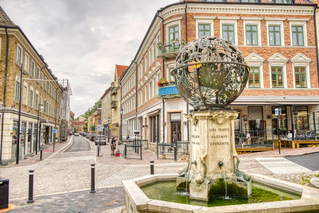 Charming street view in Helsingborg, Sweden, featuring a historic ornate fountain with a cobblestone road lined by classic architecture.