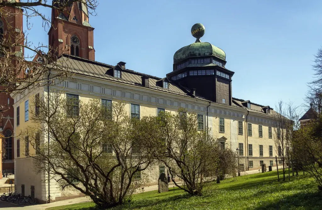 Historic Gustavianum museum in Uppsala, Sweden, showcasing its unique architecture with a large dome and adjacent church under a clear blue sky.