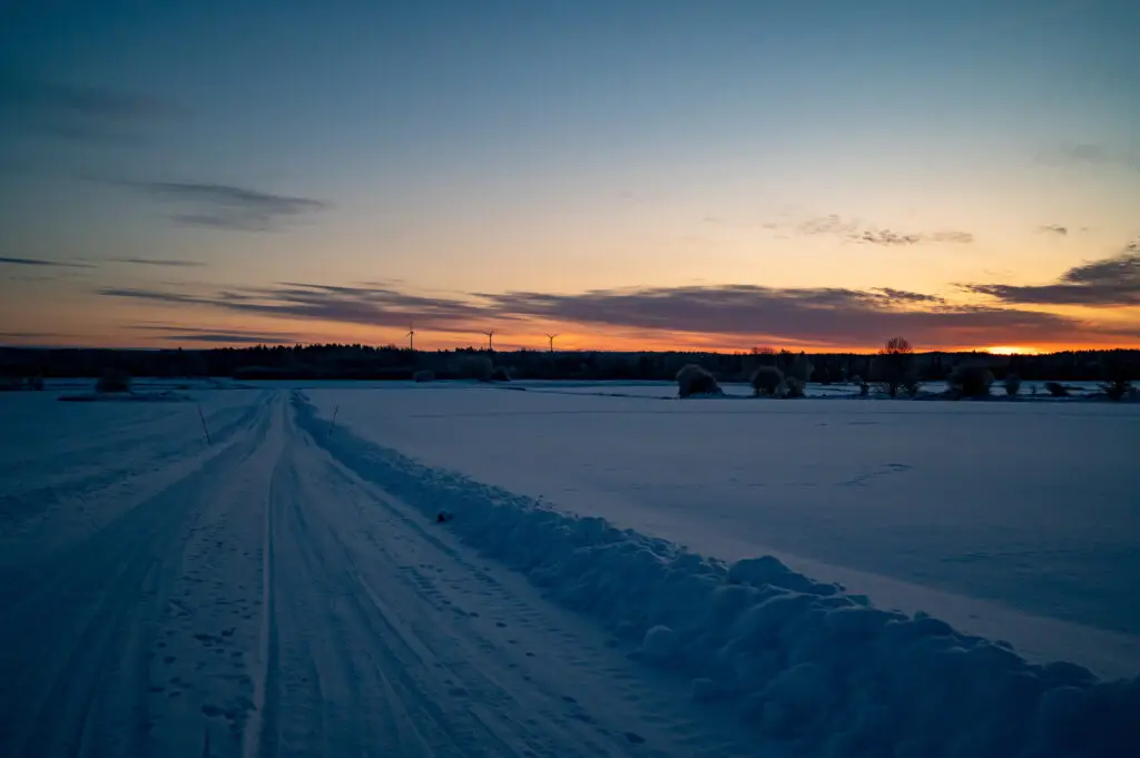 Sunrise over snowy fields in Hallsberg, Sweden, featuring a scenic winter landscape with snow-covered fields and a vibrant sky at dawn.