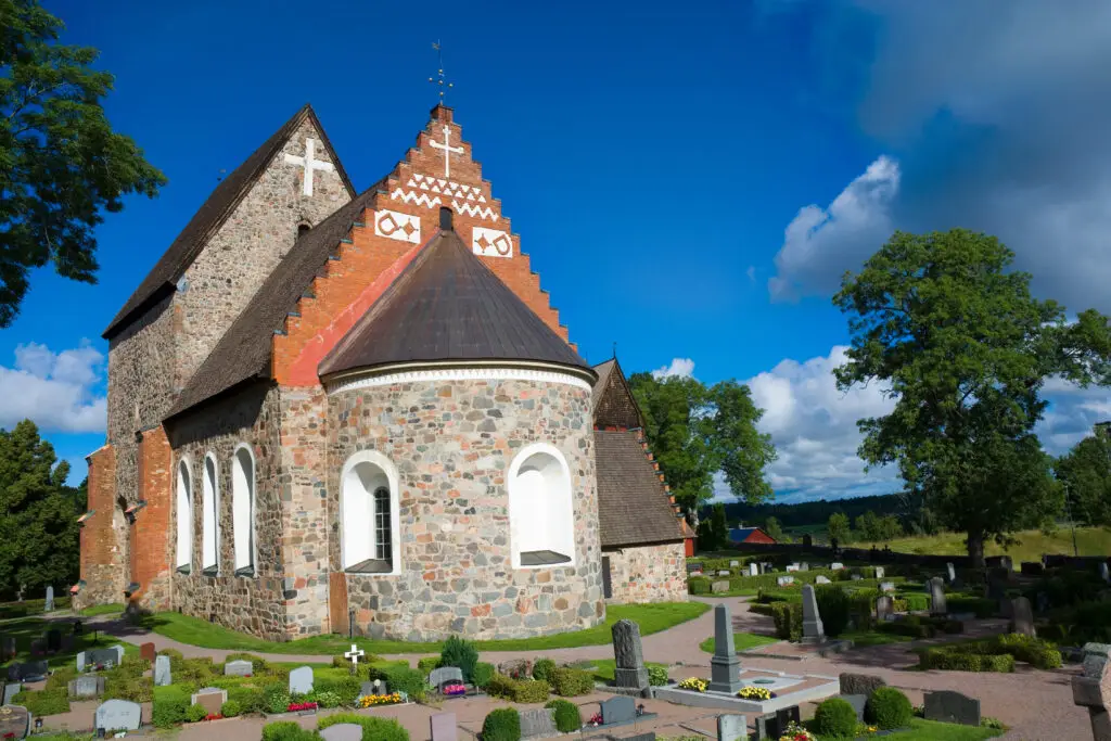 Historic Gamla Uppsala church in Sweden, a former cathedral surrounded by a lush cemetery under clear blue skies.
