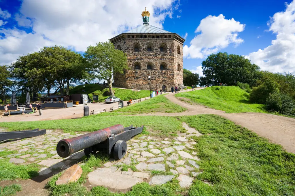 Visitors at the historical Skansen Kronan fortress in Göteborg, Sweden, with a sunny sky and an antique cannon in the foreground.