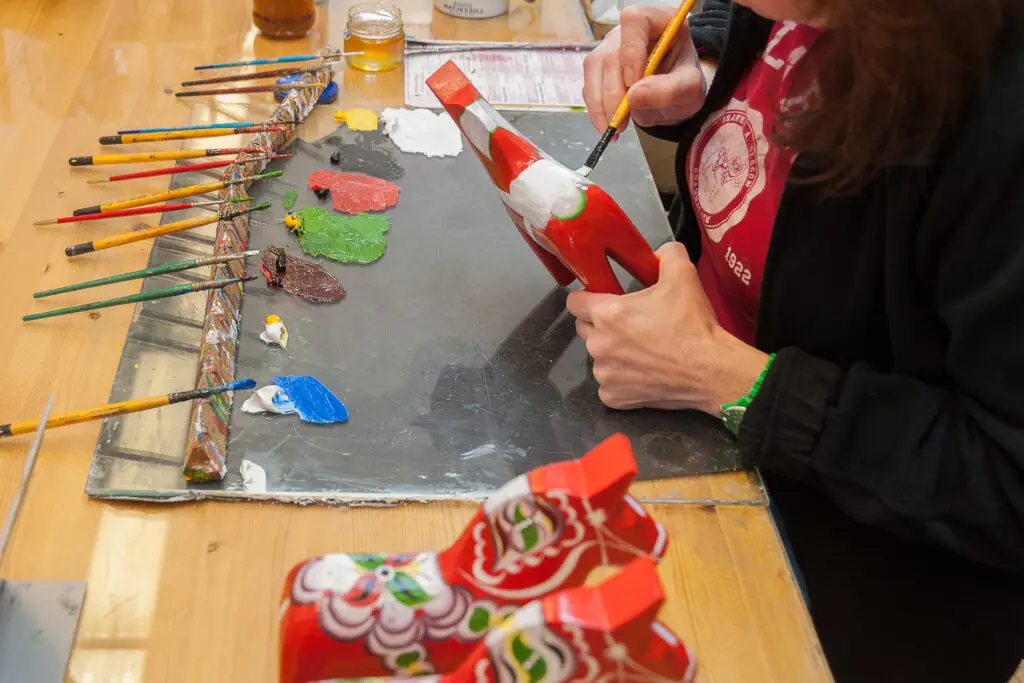 Artisan painting a traditional Swedish Dala Horse, a popular souvenir in Scandinavian tourism, surrounded by colorful paints and brushes.