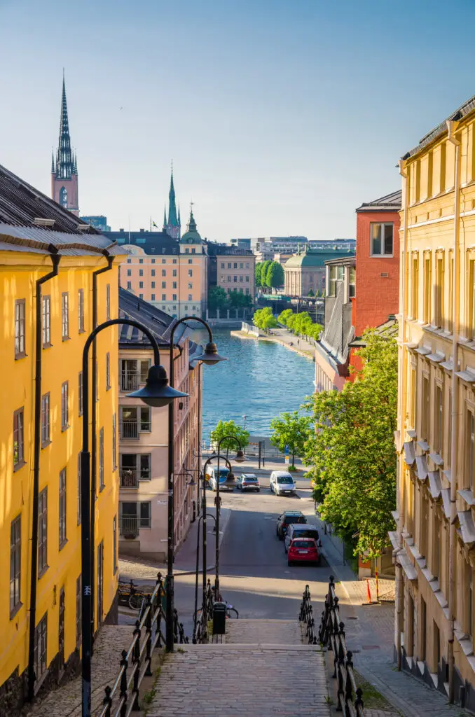 View of a picturesque narrow street and staircase leading down to Lake Malaren in Stockholm, Sweden, showcasing historic architecture and vibrant city life.
