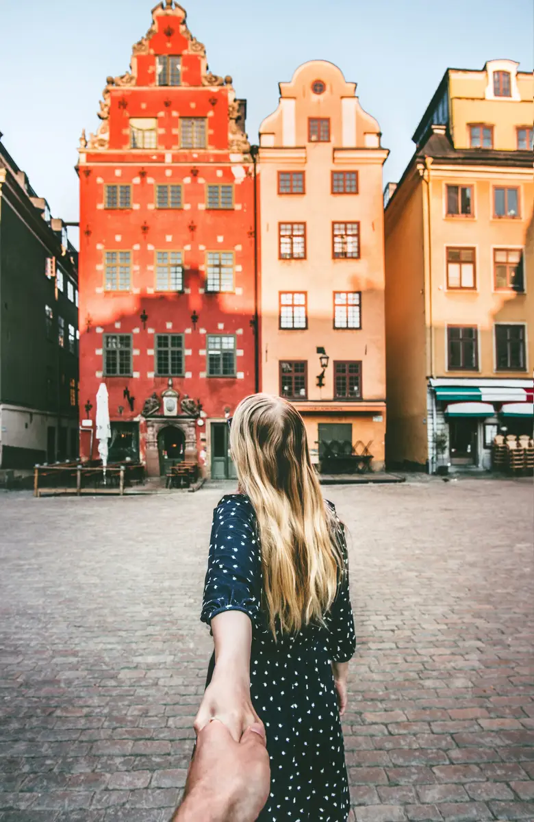 Woman leading partner by hand towards colorful historical buildings in Stortorget square, Stockholm, enhancing travel and romance in Sweden.