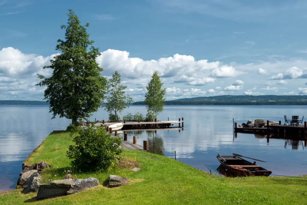 Summer morning at Lake Siljan in Sweden showing a serene view with a wooden dock, rowboat, and surrounding lush greenery, ideal for Scandinavian tourism and relaxation.